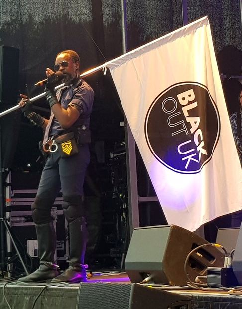 David McAlmont performing on stage beside the BLACK OUT UK flag at Croydon Pride, 2019