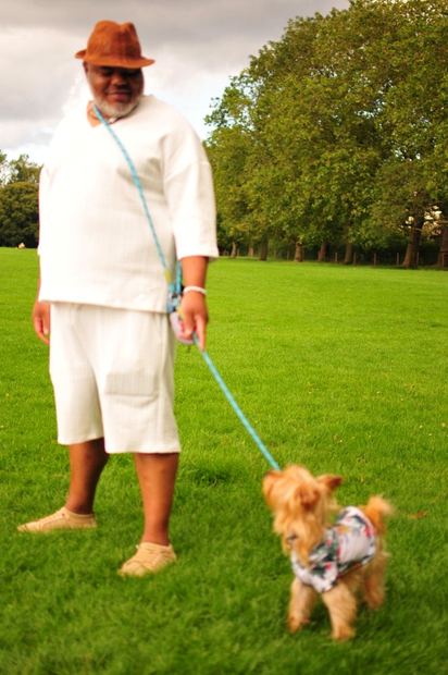 A man in a fedora and white outfit walking a small dog at the picnic