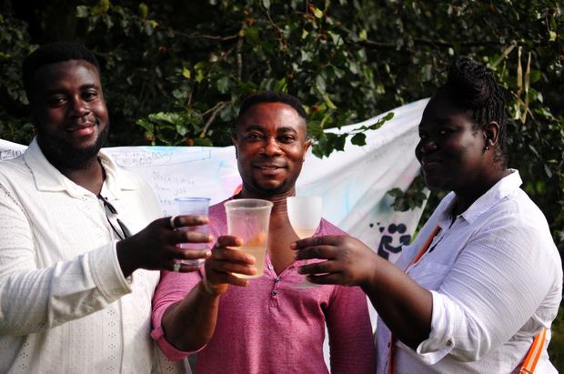 Three men in white laughing and raising glasses at the annual picnic, 2023
